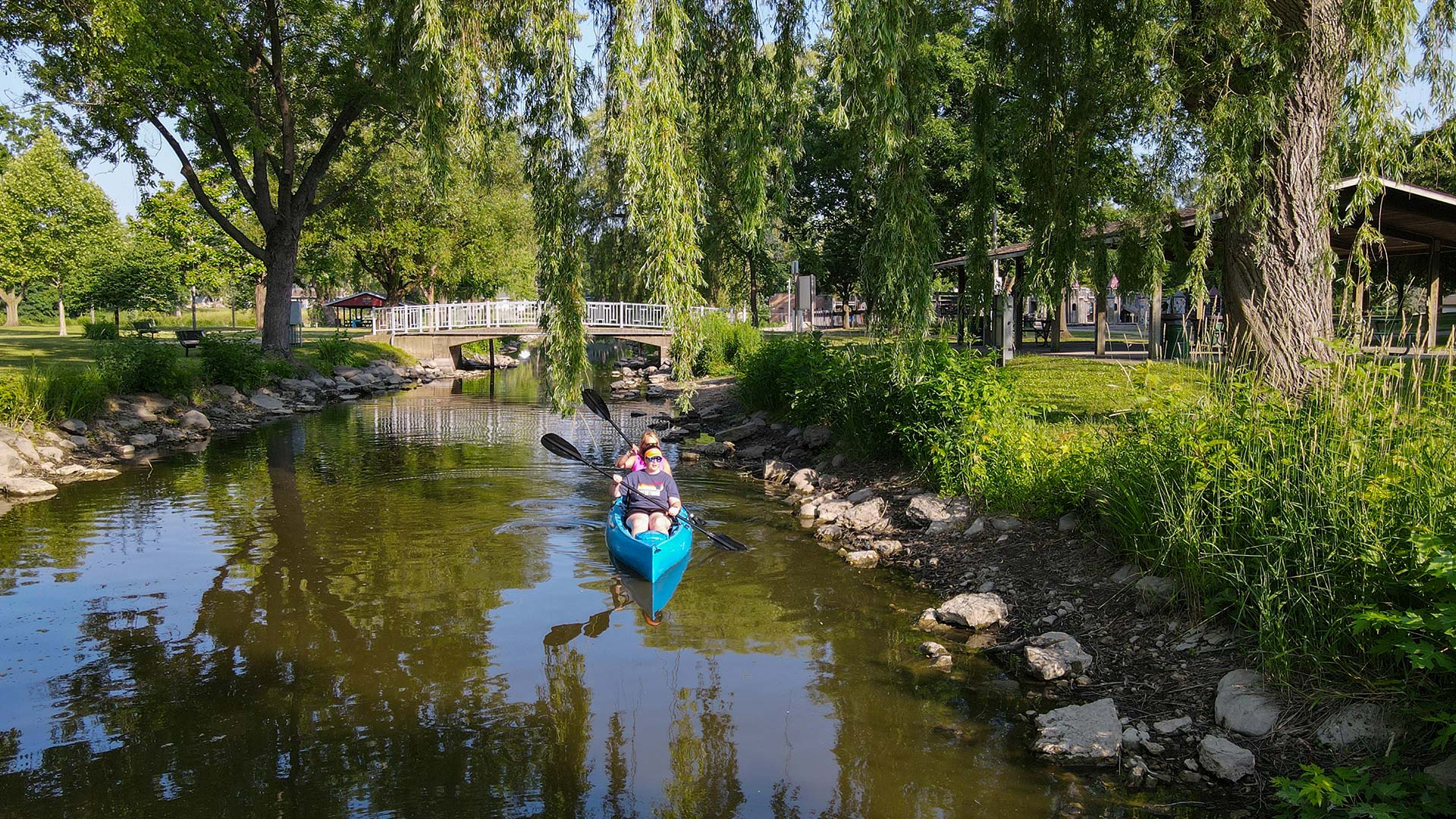 Women paddling their kayak under a hanging willow tree at Riverside Park in Watertown