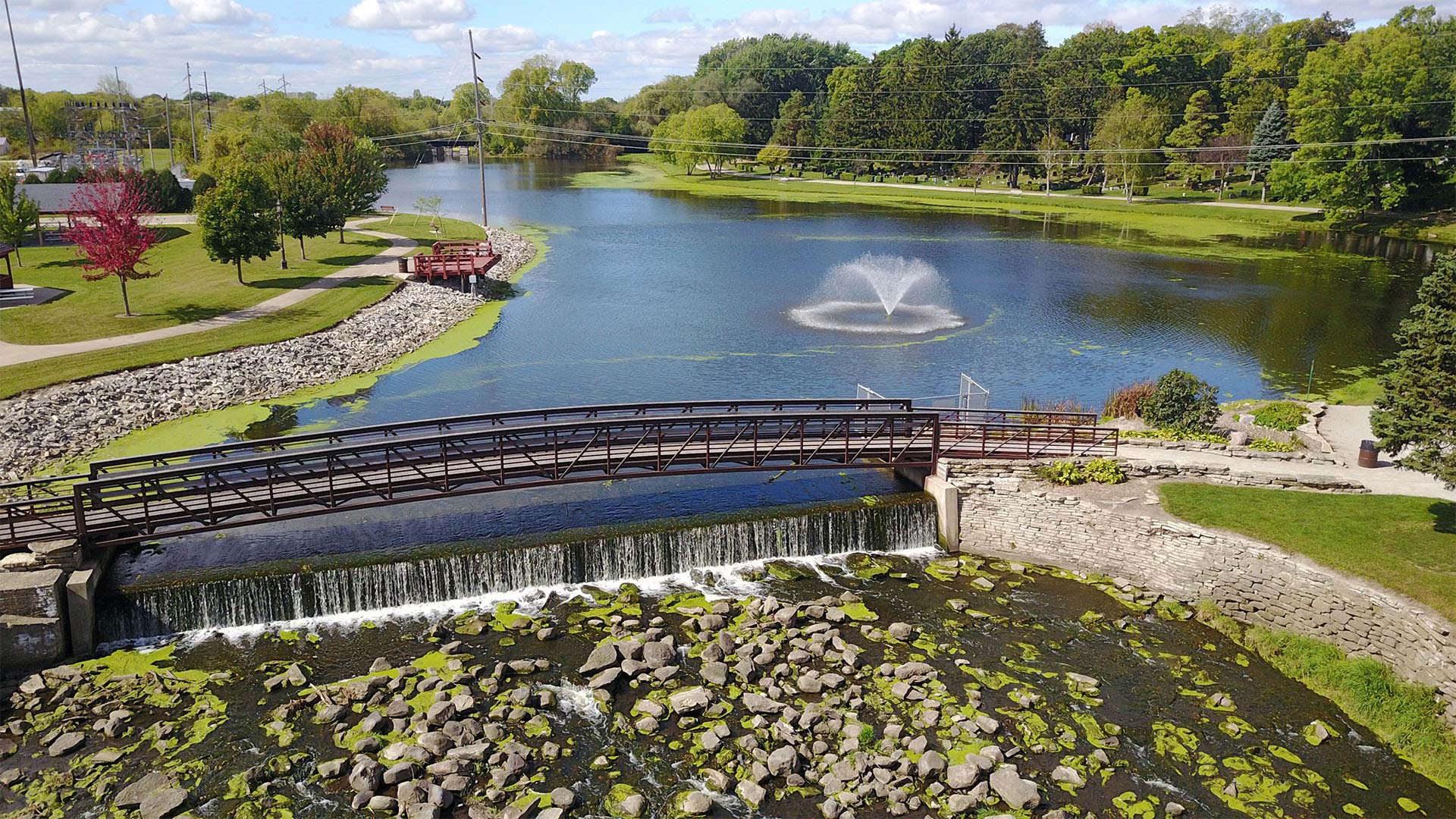Pedestrian bridge going over water with a fountain the the distance