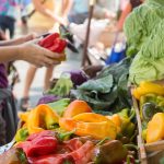 Lady holding up a vegetable at a farmers market