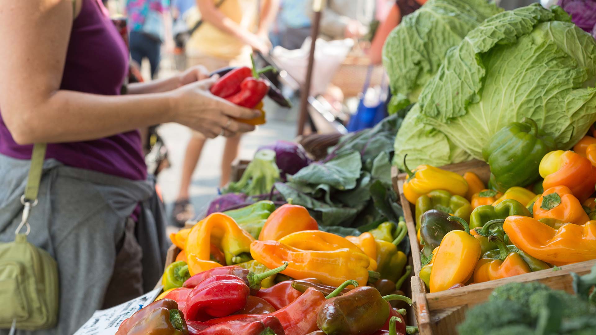 Lady holding up a vegetable at a farmers market